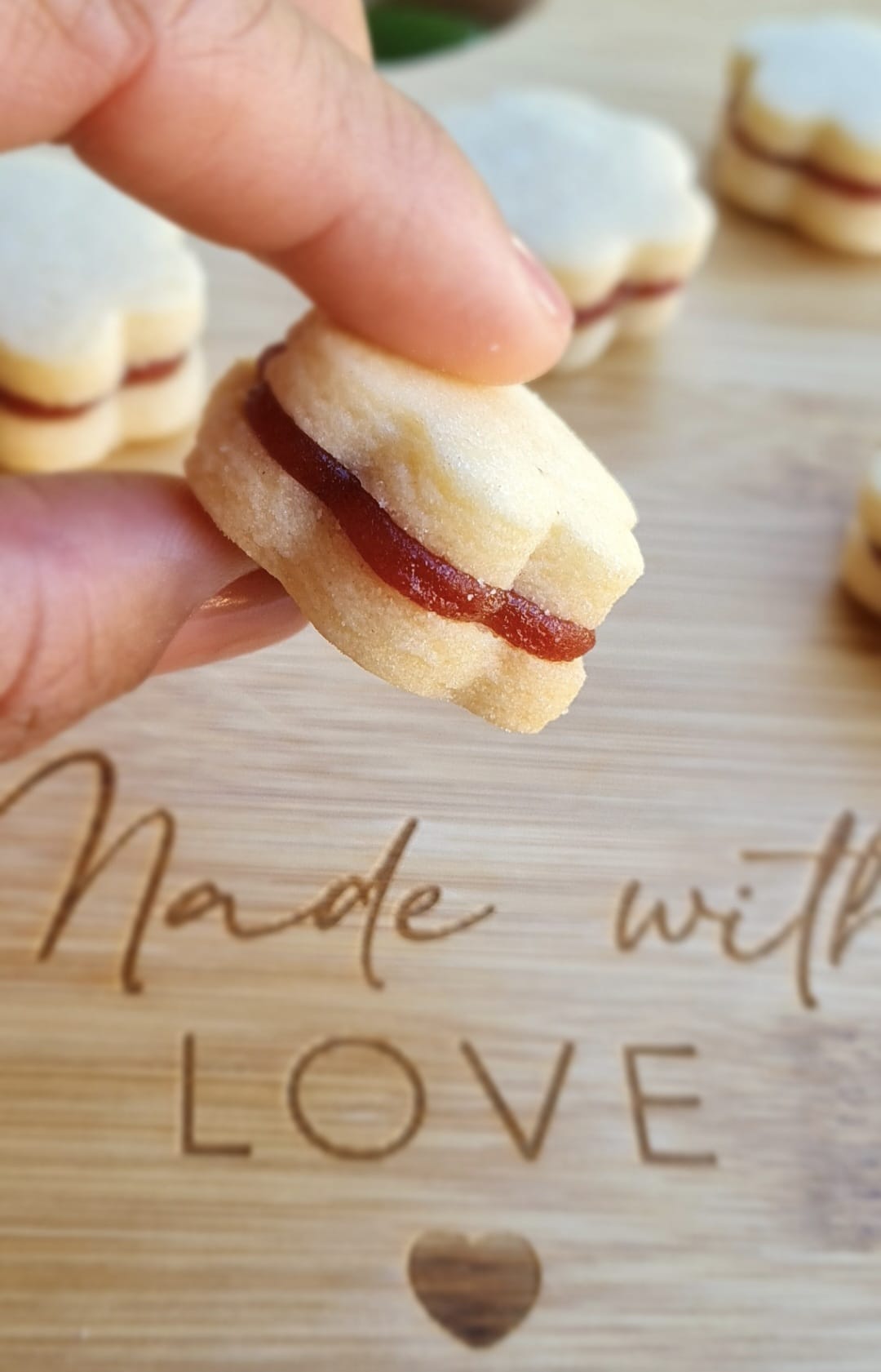 Mão segurando biscoito artesanal com tábua 'Made with Love' ao fundo